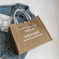 Brown jute tote bag with Hello Weekend print and white rope handles in flat lay - White Hello Weekend Print