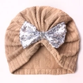 Detailed close-up of a beige baby knit hat featuring a shimmering silver sequin bow - Light Coffee