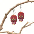 Close-up of sugar skull acrylic earrings with floral patterns on a rustic wooden branch - Red with Yellow Cross and Diamond