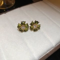 Makroansicht der dunkelgrünen Vintage-Ohrringe mit Diamanten auf weißem Samtpolster - Olivgrüner Facettierter Blumen-Stil (Silbernadel-Blume)