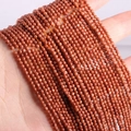 Brown-red glittering natural stone beads held in palm showcasing texture and details - Gold Sandstone