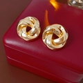 Close-up of golden knotted metal stud earrings on a luxury red leather jewelry box - Gold