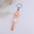 Vue détaillée des perles en silicone orange, du charme fleur et du porte-clés à pompon orange - Rose Bonbon
