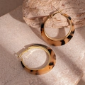 Detailopname van luipaard hars oorringen met gouden accenten op een stenen basis - Bruine luipaard creolen