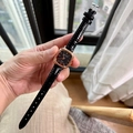 Square rose gold watch with black leather strap and Roman numerals held in hand - Black