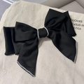 Detail view of large black satin bow hair clip with fine pearl edges on canvas background - Black