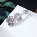Detailed close-up of a silver violin brooch with pavé rhinestones on white marble - Silver