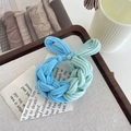 Braided blue and mint green elastic hair tie placed on a book for hair styling - Blue Green