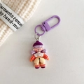 Detail van poppen-sleutelhanger met paarse hoed en gestreept shirt op witte textuur - Paars