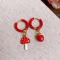 Detailopname van asymmetrische emaille oorbellen met rode paddenstoel- en appelhangers - Oorring - Goud - Rood - Paddestoel - Appel