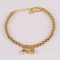 Pulsera de cuentas de acero de titanio dorado con dijes de corazón y loto sobre fondo blanco - Dos Generaciones Juntas (Vaina de Loto)