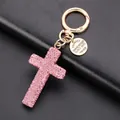 Pink rhinestone cross keychain with gold alloy base and leather cord on black background - Pink