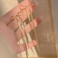 Close-up of hand holding golden bow-knot earrings with long hanging metal tassels - Bow Combination / Gold