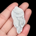 White turquoise leaf pendant with gray veins held by hand against black background - Howlite
