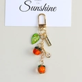 Macro shot of orange persimmon fruit keychain with green leaf and handmade metal tag - Persimmon Pendant