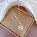 Primer plano de collar dorado con colgante cuadrado de gemas sobre fondo de seda - Blanco (E418)