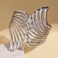 Macro shot of silver hollow wing cuff bracelet on stone with warm lighting - Silver