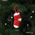 Handgemaakte rood-witte gehaakte kerstsok hanger aan een tak van een groene dennenboom - Kerstsok