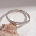 Detalle macro del brazalete geométrico plateado con textura vertical sobre base de piedra - Brazalete abierto con textura vertical / Plateado