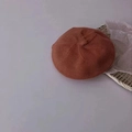 Knitted baby beret hat in rust red color on a minimalist woven tray display - Caramel color