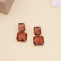 Macro detail of amber crystal drop earrings with golden square stone claw setting - Coffee