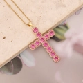 Close-up of gold cross necklace featuring pink round-cut cubic zirconia on a stone tile - Rose Red