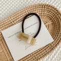 Detail of a brown acetate geometric hair tie with handmade gold lettering on white card - Khaki Pattern