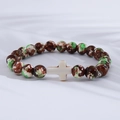 Close-up of wooden beads and turquoise cross bracelet on soft white fabric background - Brown Green White Mottled White Cross