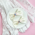 Détail de pinces à cheveux en satin crème avec strass en cœur bleu sur une assiette - Beige
