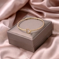 Detail of a thin gold heart-shaped bangle on gray jewelry box and pink silk fabric - Heart Style (S276-1)