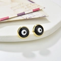 Detailed view of Evil Eye stud earrings with gold rim on a white textured display - Black