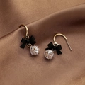 Detail von vergoldeten Schleifenohrringen mit schwarzem Matt-Finish und Kristallperle auf Satin - Schwarze Schleife/Goldener Haken