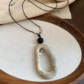 Détail du collier pendentif en acrylique marbré sur fond de plateau en bois rustique - Cordon Noir Motif Marbre Ovale