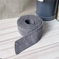 Macro detail of charcoal grey wool belt roll for winter coats on a wooden surface - Gray