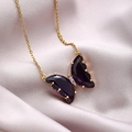 Close-up of gold butterfly necklace with purple crystal wings on soft satin background - Purple