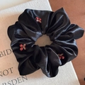 Detail of a black velvet hair ring featuring red cherry accents on a minimalist book background - Red Cherry Black Velvet Scrunchie