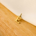 Detailed view of a gold-plated letter E pendant on white fabric and light wood background - 14k Letter - E (letter Height 1cm)