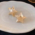 Close-up of high-polish golden star stud earrings on a decorative white porcelain tray - Gold Star Shape
