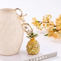 Dettaglio del portachiavi a forma di ananas con strass e moschettone dorato su vaso bianco - Portachiavi / Giallo