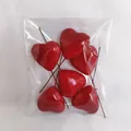 Macro view of six shiny red heart cake toppers with brown sticks in plastic wrap - 50mm (Pack)