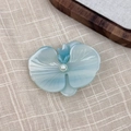 Primer plano de pinza de pelo orquídea azul con perla sobre fondo de lino - Azul