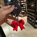 Llavero con lazo rojo metálico y anillo plateado mostrado a mano en una joyería - Lazo Brillante Rojo
