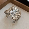 Close-up of vintage floral hollow metal cuff bracelet with detailed filigree patterns - Silver