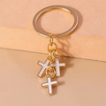 Macro detail of three white enamel cross charms on a golden flat metal key ring - White