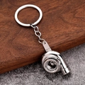 Detail of polished silver zinc alloy turbocharger model keychain on wood surface - White K/Silver