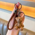 Detail van een bruine hars teddybeer sleutelhanger met geweven riem en metalen ring - Bruin