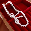 Detailed shot of bow-shaped pearl pendant and adjustable gold clasp on red velvet - Large White Imitation Pearl Bow Necklace
