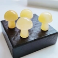 Set of four polished yellow natural stone mushroom ornaments on a black textured box - Yellow Jade