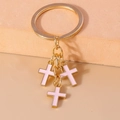 Close-up of golden keychain featuring three pink enamel crosses with polished metal rings - Pink