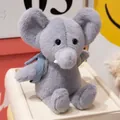 Plush grey elephant toy with light blue backpack accessory sitting on a cream box - Elephant With Backpack / 21cm